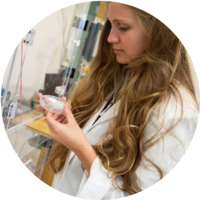 A female student wearing a lab coat examines a test sample.